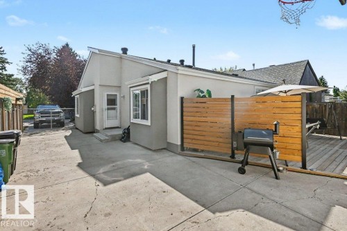 Exterior featuring light gray siding, white trim, a concrete patio, and a wood deck with privacy screening - 8708 25A Avenue Nw, Edmonton, AB 