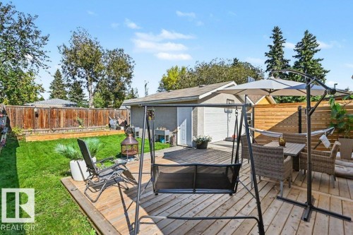 Expansive backyard with a wood-finish deck, lush lawn, wood fencing, and a detached garage featuring a white overhead door - 8708 25A Avenue Nw, Edmonton, AB 