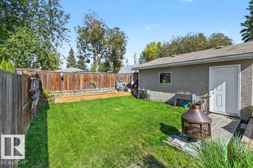 Expansive backyard featuring a manicured lawn, wood fencing, and a detached building with a shingle roof - 8708 25A Avenue Nw, Edmonton, AB 