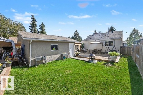 Spacious backyard featuring a manicured lawn, a detached stucco-finish garage, a large wooden deck, and a wood privacy fence - 8708 25A Avenue Nw, Edmonton, AB 