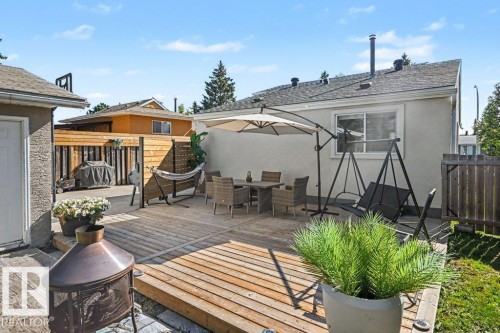 Expansive wood-finish deck with a privacy fence, stucco exterior, and a built-in fire pit - 8708 25A Avenue Nw, Edmonton, AB 