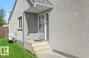 Stucco exterior featuring a covered porch entry, concrete steps, and a white screen door - 8708 25A Avenue Nw, Edmonton, AB 