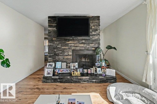 Fireplace featuring a stone facade and hearth, wood-finish flooring, and light-colored walls - 8708 25A Avenue Nw, Edmonton, AB 