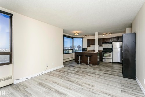 Expansive open-concept living area featuring wood-finish flooring, large windows, recessed and track lighting, a breakfast bar, and stainless steel appliances - #815 10160 114 St Nw, Edmonton, AB 