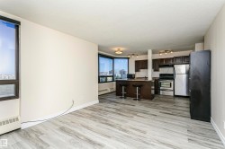 Expansive open-concept living area featuring wood-finish flooring, large windows, recessed and track lighting, a breakfast bar, and stainless steel appliances - 