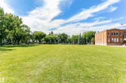 Expansive green space featuring a large grassy area, mature trees, and a brick building with multiple windows - 