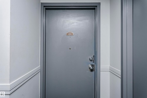 Gray entry door with a brass-finish number plaque, peephole, and silver-tone hardware - #815 10160 114 St Nw, Edmonton, AB 