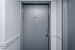 Gray entry door with a brass-finish number plaque, peephole, and silver-tone hardware - 