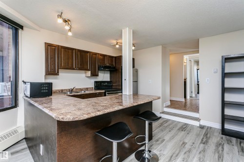 Kitchen featuring dark wood cabinetry, a breakfast bar with stone-finish countertop, and integrated appliances - #815 10160 114 St Nw, Edmonton, AB 