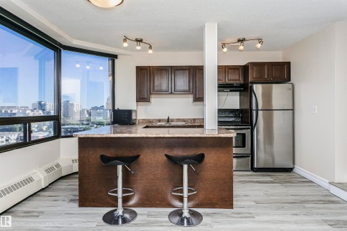 Kitchen featuring stainless steel appliances, dark wood-finish cabinetry, and a breakfast bar with a stone-finish countertop - #815 10160 114 St Nw, Edmonton, AB 