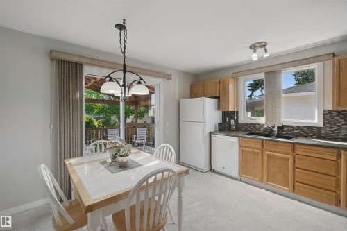 Eat-In Kitchen with light wood-finish cabinetry, a patterned tile backsplash, and a sliding glass door leading to an outdoor deck - 11439 144 Avenue Nw, Edmonton, AB 