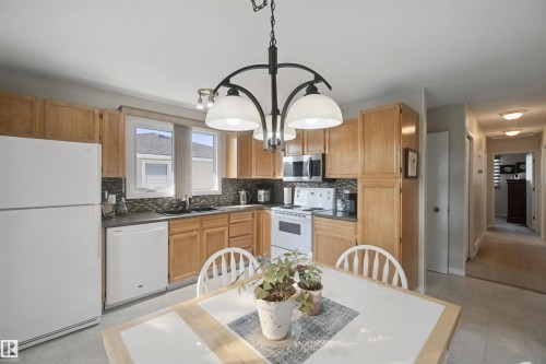 Eat-In Kitchen featuring wood cabinetry, dark countertops, white appliances, and a tiled backsplash - 11439 144 Avenue Nw, Edmonton, AB 