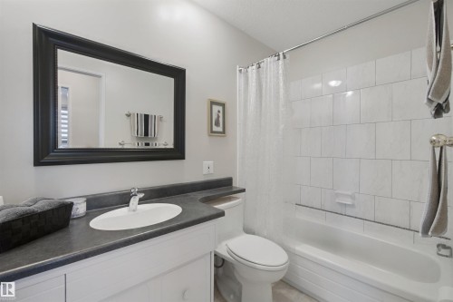 White vanity with a dark countertop, an oval undermount sink, and a framed mirror - 11439 144 Avenue Nw, Edmonton, AB 