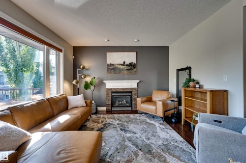 Hardwood flooring, a built-in fireplace with stone surround, a white mantel, and a large window - 2203 Warry Loop Sw, Edmonton, AB 