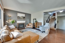 Living area featuring wood-finish flooring, a fireplace with a stone surround, and a staircase with dark wood railings - 