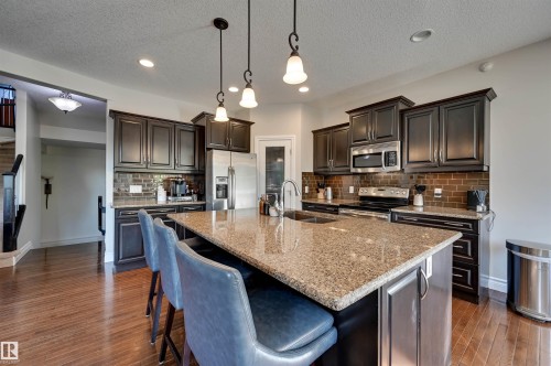 Kitchen featuring a large island with a stone countertop, dark wood-finish cabinetry, stainless steel appliances, and wood-finish flooring - 2203 Warry Loop Sw, Edmonton, AB 