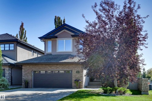 Two-story residence featuring stucco and stone veneer exterior, a dark shingle roof, attached garage with frosted-panel door, and a concrete driveway - 2203 Warry Loop Sw, Edmonton, AB 