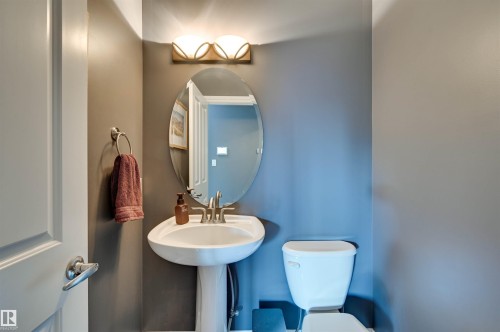 Pedestal sink with a polished chrome faucet, oval wall mirror, and a wall-mounted light fixture - 2203 Warry Loop Sw, Edmonton, AB 