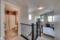 Hallway featuring a dark wood staircase with wrought iron balusters, leading to a loft space with vaulted ceilings and light-toned carpeting - 