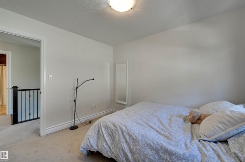 Carpeted room with white walls, a flush-mount ceiling light, and a doorway opening to a hallway with black metal railings - 2203 Warry Loop Sw, Edmonton, AB 