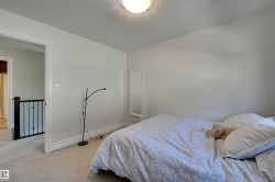 Carpeted room with white walls, a flush-mount ceiling light, and a doorway opening to a hallway with black metal railings - 