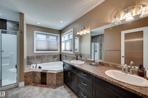 Dual vanity with integrated sinks, a corner soaking tub, a separate shower enclosure, and two windows with blinds - 2203 Warry Loop Sw, Edmonton, AB 