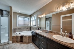 Dual vanity with integrated sinks, a corner soaking tub, a separate shower enclosure, and two windows with blinds - 
