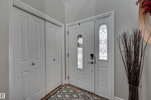Entryway with a white paneled door featuring decorative glass inserts, a white paneled sidelight, and double bi-fold closet doors - 2203 Warry Loop Sw, Edmonton, AB 