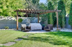 Expansive lawn area with stepping stones, a wooden pergola, a paved patio, and a privacy fence with mature trees - 