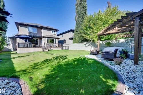 Expansive backyard featuring a manicured lawn, a multi-level deck, and a wooden pergola over a stone-filled patio - 2203 Warry Loop Sw, Edmonton, AB 