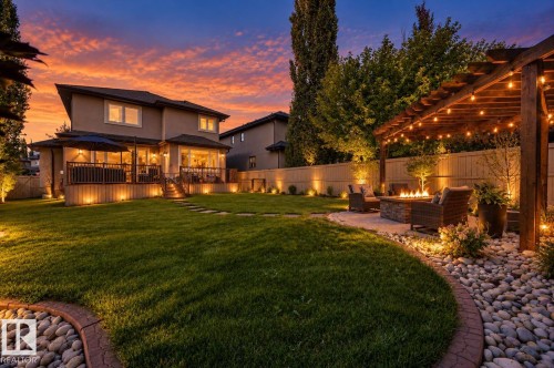 Expansive backyard featuring a manicured lawn, a multi-level deck, stepping stone pathway, and a pergola-covered patio with a built-in fire pit - 2203 Warry Loop Sw, Edmonton, AB 