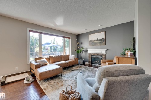 Hardwood flooring, large picture window, stone-front fireplace with mantel, recessed lighting, and a neutral color palette - 2203 Warry Loop Sw, Edmonton, AB 