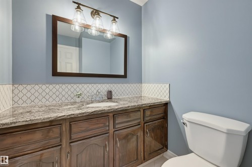 Vanity with wood-finish cabinetry, stone countertop, integrated sink, and an arabesque tile backsplash - 30 Gariepy Crescent Nw, Edmonton, AB 