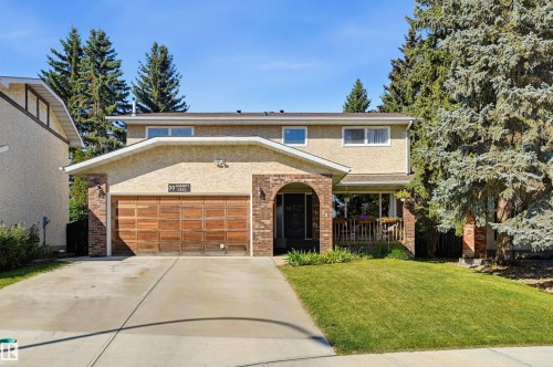 Stucco exterior with brick accents, wood-paneled garage door, and a covered porch - 30 Gariepy Crescent Nw, Edmonton, AB 