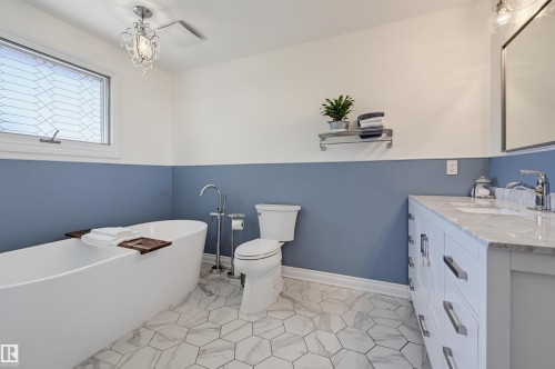 Freestanding soaking tub, hex tile flooring, single vanity with countertop, chrome fixtures, and crystal chandelier - 30 Gariepy Crescent Nw, Edmonton, AB 