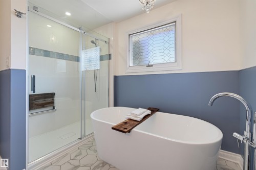 Freestanding oval soaking tub with floor-mounted faucet, glass-enclosed shower with tile accent band, and hexagonal floor tiling - 30 Gariepy Crescent Nw, Edmonton, AB 