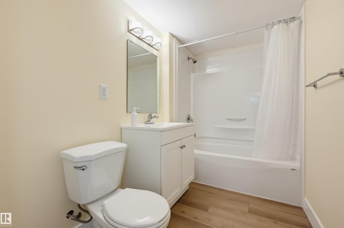 Wood-finish flooring, white vanity with integrated sink, chrome faucet, wall-mounted mirror, and a white shower/tub combination - 30 Gariepy Crescent Nw, Edmonton, AB 