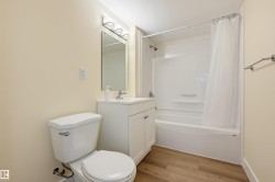 Wood-finish flooring, white vanity with integrated sink, chrome faucet, wall-mounted mirror, and a white shower/tub combination - 
