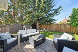 Expansive backyard featuring a wood deck, lawn area, mature trees, and privacy fencing - 