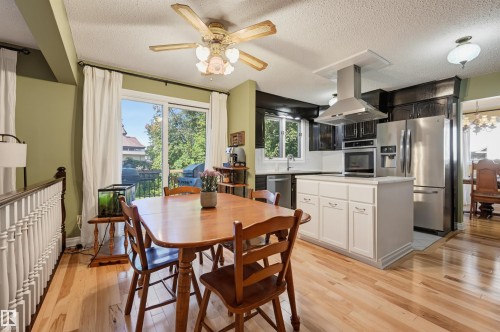 Kitchen featuring dark wood cabinetry, stainless steel appliances, a center island with white paneling, and wood-finish flooring - 30 Gariepy Crescent Nw, Edmonton, AB 