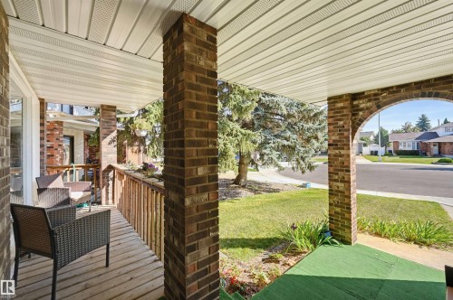 Covered front porch featuring brick columns, wood railing, and plank flooring - 30 Gariepy Crescent Nw, Edmonton, AB 
