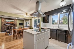 Kitchen island with integrated cooktop and stainless steel range hood, contrasted by dark cabinetry and light countertops - 