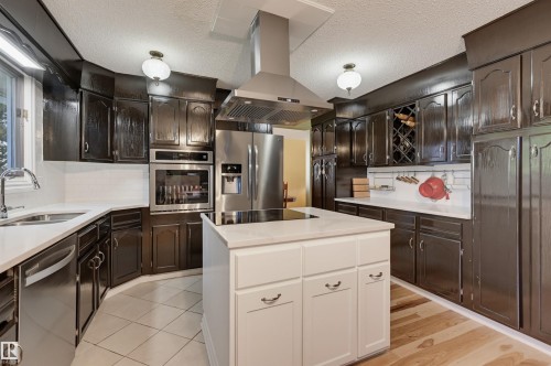 Kitchen featuring an island cooktop, stainless steel appliances, dark wood-finish cabinetry, light countertops, and mixed flooring - 30 Gariepy Crescent Nw, Edmonton, AB 