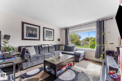 Large window with outdoor scenery, recessed window blind, wood-finish flooring, and light-toned walls - 16012 98 Avenue Nw, Edmonton, AB 