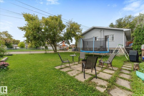 Expansive grassy yard with mature trees, a concrete paver patio, and a light-colored siding exterior - 16012 98 Avenue Nw, Edmonton, AB 