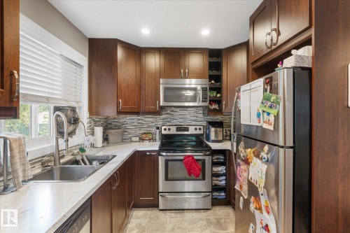 Kitchen featuring stainless steel appliances, wood-finish cabinetry, a mosaic tile backsplash, and light-toned countertops - 16012 98 Avenue Nw, Edmonton, AB 
