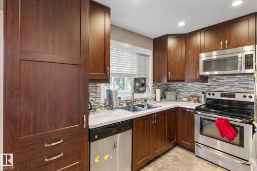 Dark wood-finish cabinetry, stainless steel appliances, mosaic tile backsplash, white countertops, and recessed lighting - 16012 98 Avenue Nw, Edmonton, AB 
