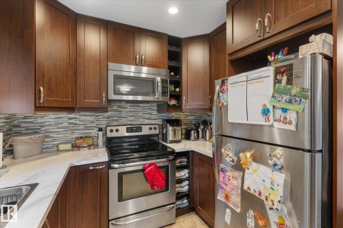 Kitchen featuring dark wood-finish cabinetry, stainless steel appliances, a mosaic tile backsplash, and light-toned countertops - 16012 98 Avenue Nw, Edmonton, AB 