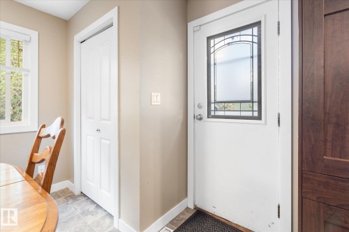 Entry door with decorative glass insert, paneled bifold closet door, wood-finish cabinetry, and tile flooring - 16012 98 Avenue Nw, Edmonton, AB 
