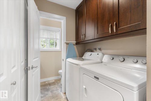 Laundry area with wood-finish cabinetry, a window with blinds, and tile flooring - 16012 98 Avenue Nw, Edmonton, AB 
